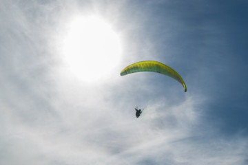 Parapente color verde volando alto con sol de fondo en dia nublado
