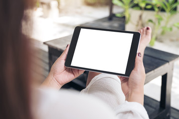 Mockup image of a woman sitting and holding black tablet pc with blank white desktop screen , feeling relaxed with sand and beach background