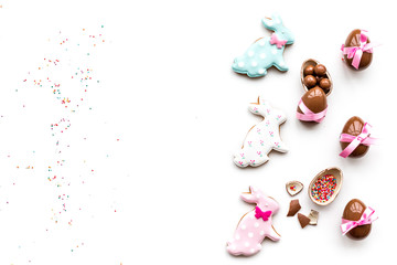 Fototapeta na wymiar Sweets for Easter table. Chocolate eggs near cookies in shape of Easter bunny on white background top view copy space