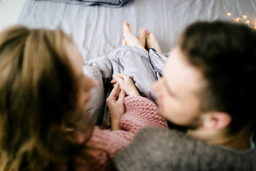 A loving couple looks each other and holding hands while sitting in bed at home together. Artwork. Selective focus on the hands - 191134247
