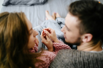 A loving couple looks each other and holding hands while sitting in bed at home together. Artwork. Selective focus on the hands - 191134433
