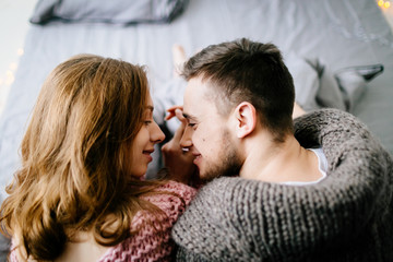Falling in love. A beautiful young loving couple looks each other and smiling while sitting in bed at home together. Artwork
