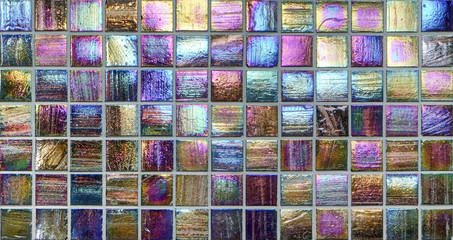 Colorful square metallic tiles on a wall or floor. Blue, green, teal, yellow, orange, purple reflective tile pattern. Shiny tile pattern with purple, teal, green, blue, yellow, gold and orange.