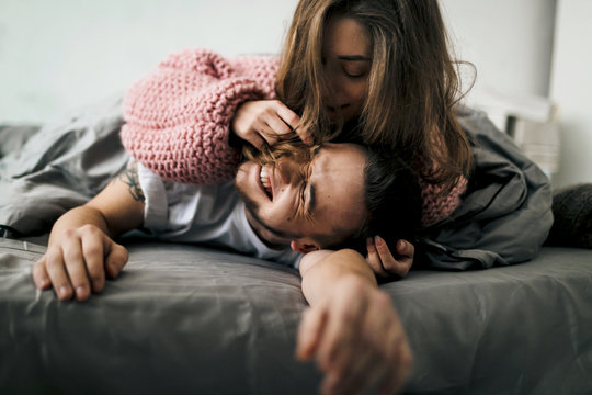 Smiling young couple playing in bed at home. Artwork