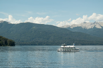 Paisaje de un lago azul con barco blanco y monta&ntilde;as de fondo