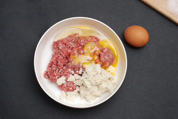 Minced meat in Bowl with Spices and Egg on Dark Background. Top view, Black Background.