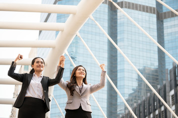 Two Asian business women raising arms and smiling with urban scene background. Teamwork and success concept