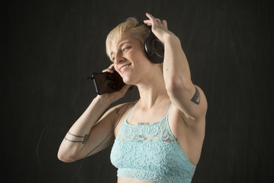 Young blonde woman in blue camisole dancing with headphones on.
