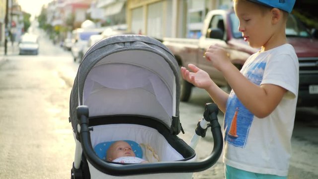 Slow motion shot of a boy with baby in pram. Elder brother looking after junior sister outdoor