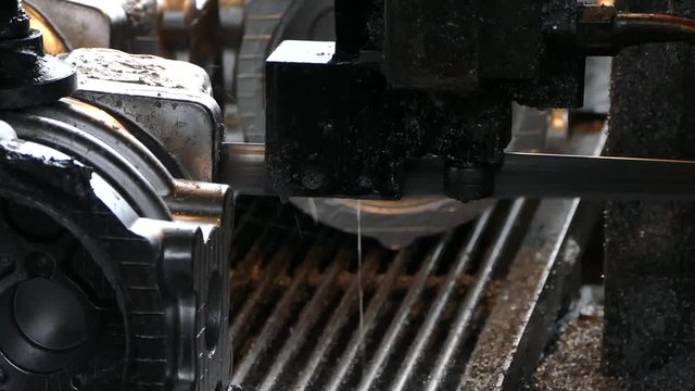 Cutting of aluminum products with a heavy-duty saw. Production of aluminum billets in the factory. The locksmith works behind the machine.