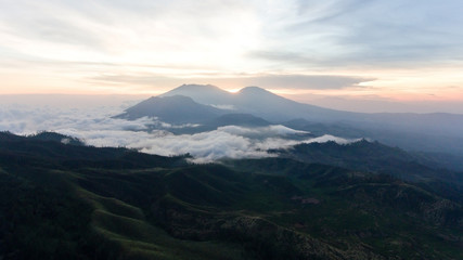 Naklejka na ściany i meble Beautiful sunset in the mountains on Jawa island, Indonesia. Aerial view of mountains landscape under sky with clouds, rainforest.
