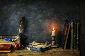 Classic still life with vintage books placed with old eye glasses,pipe,illuminated candle and antique ink with feather on rustic wooden background