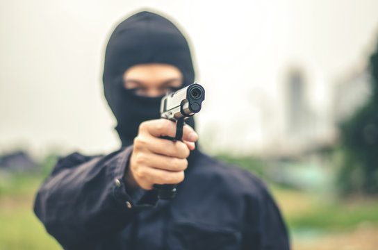 Mask thief in balaclava with holding gun ,Outlaw bad man  hold a gun pointing the target , robber in black hood holding gun and pointing to victim