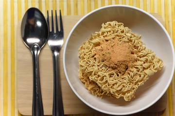 Instant noodles flavored soup in bowl with fork. On the second sheet of wood