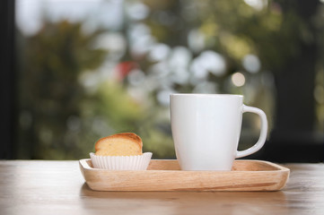 A white cup of coffee and crispy butter bread on wooden plate on wooden table with bokeh background.
