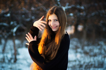 A fashion model in a black dress in the winter in the yard puts on a photo shoot