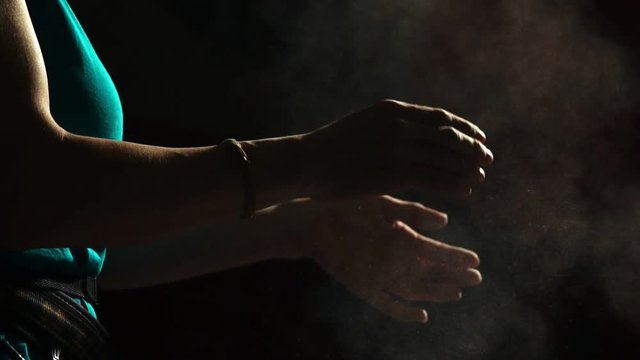 Close-up on a black background with a hand of a professional balder. Apply chalk on your hands against slipping. Cotton and dust scattered in different directions. Sport competitions. Backlight. Slow