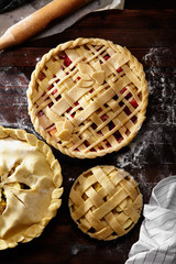 Pie crust design ideas - various ways of pie decoration with lattice and leaves. Apple, strawberry and raspberry pies uncooked on dark wooden background.