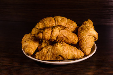 Plate with fresh croissants on a dark wooden table