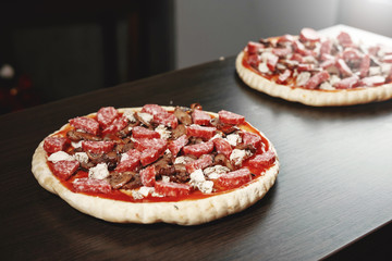 pizza cooking, meat of chiken, sausage salami, thick dough,  pizza crust, pizza is on a dark table, pizza with chicken and sausage salami, cooking process, mushrooms,  Champignon