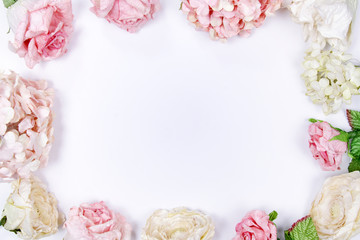 Frame made of pink and beige roses, hydrangea, green leaves, branches on white background. Flat lay, top view. Wedding's background. Valentines day background with copy space.