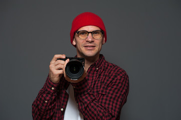 Cute hipster man in stylish clothes photographer holds camera and posing on gray gbackground