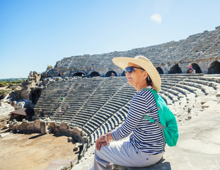 Mature beautiful woman traveler, sits on the steps of the amphitheater in admiring the view. Travel...
