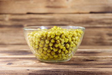 Canned green peas in glass bowl on wooden table