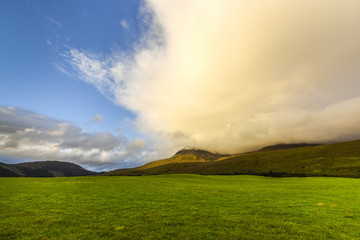Idyllic meadow with mountains in the background, blue sky and orange clouds in appealing sunset atmosphere, Highlands, Scotland, Great Britain