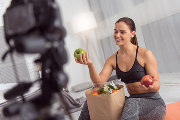 Tasty apples. Beautiful joyful athletic young woman smiling and having a packet with vegetables and...