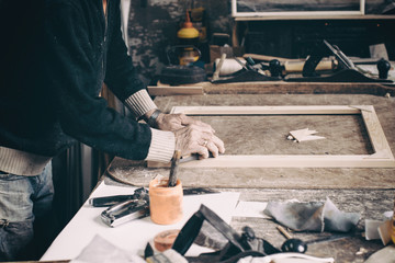 An elderly desk is working in his workshop on the table, making a stretcher for the picture.