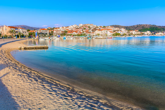 Fototapeta Rogoznica beach tourist resort. / Coastline view at marble Rogoznica town scenery with sandy beach in foreground, Mediterranean Croatia.