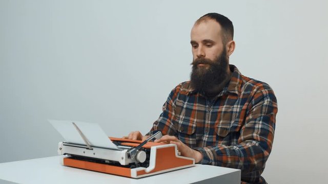 Hipster sitting at table and typing with a red vintage typewriter