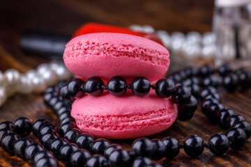 Macaroons of cookies of pink shades on a wooden background with makeup products.