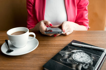 Fototapeta na wymiar female hands with a black phone, close-up, background of a cup of coffee, table, notebook. Business lunch.