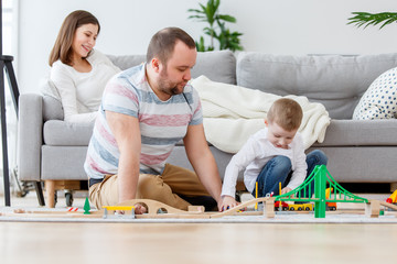 Photo of father playing with son in toys sitting on floor, sitting next to pregnant mother