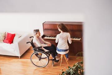 A girl with grandmother in wheelchair playing the piano.