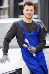 Automechaniker  / Automechatroniker vor einer Auto-Werkstatt 