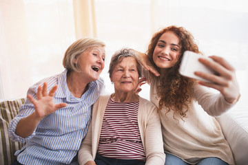 A teenage girl, mother and grandmother with smartphone at home.