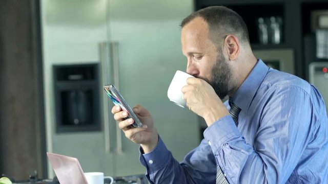 Businessman texting on smartphone and drinking coffee by table at home 
