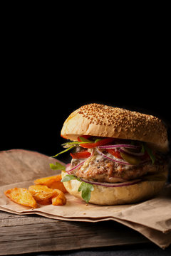 appetizing hamburger with blue onions, tomatoes and greens on a wooden plank