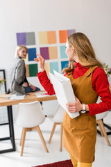 Obraz premium attractive magazine editor with folder pointing at colleague and color palette on wall behind