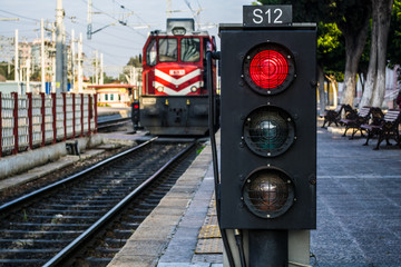 traffic light shows red signal on railway; railway station and the train is coming
