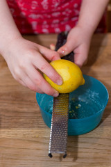 Little girl grating zest of organic lemon on kitchen table