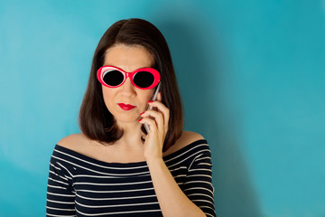Woman in blue striped top and red sunglasses talking on a smartphone.