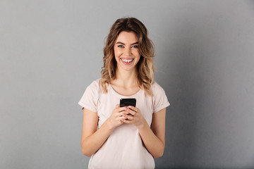 Smiling woman in t-shirt holding smartphone and looking at camera