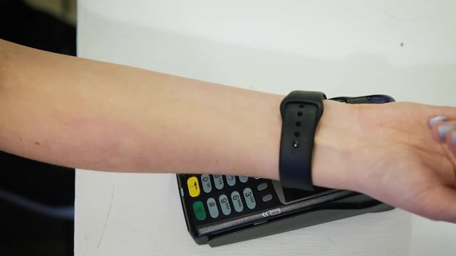 Customer paying with NFC technology by smart watch contactless on terminal in modern cafe.