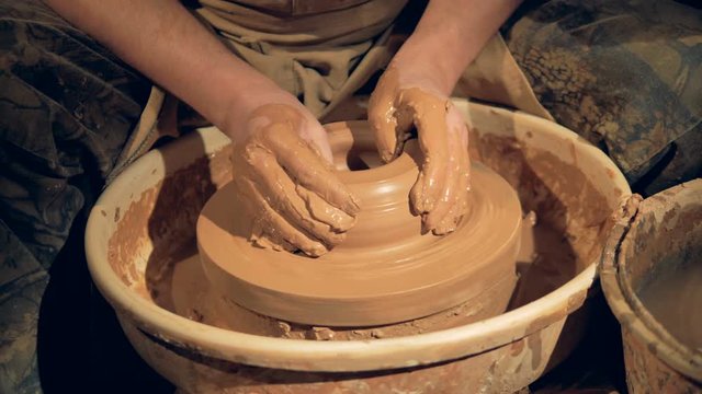 Potters hands make a wide low bowl on a wheel. 