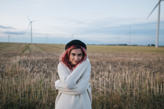beautiful happy girl in white sweater standing in field with wind turbines