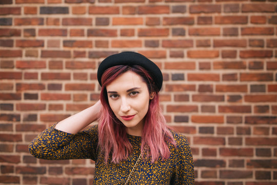 portrait of beautiful girl with pink hair in trendy hat posing at wall